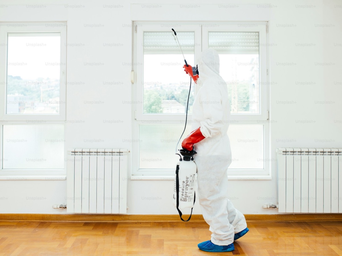 Pest control technician spraying treatment along the foundation of a residential property